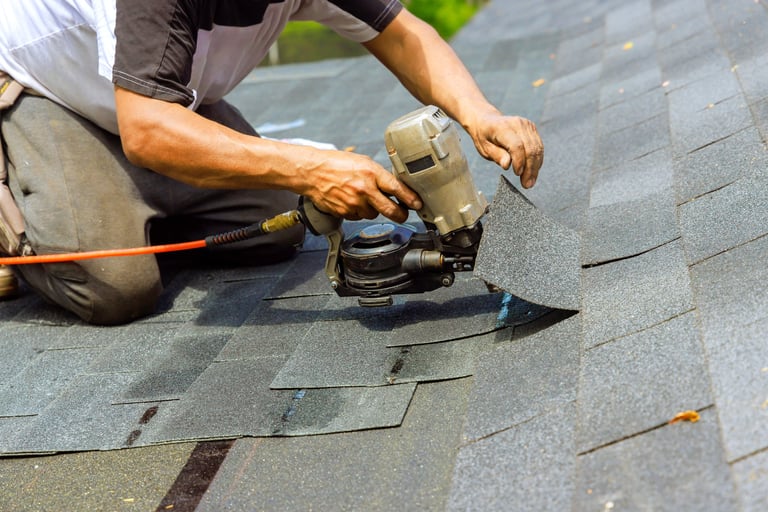 Construction roofer installing new bitumen shingles with pneumatic air nail gun