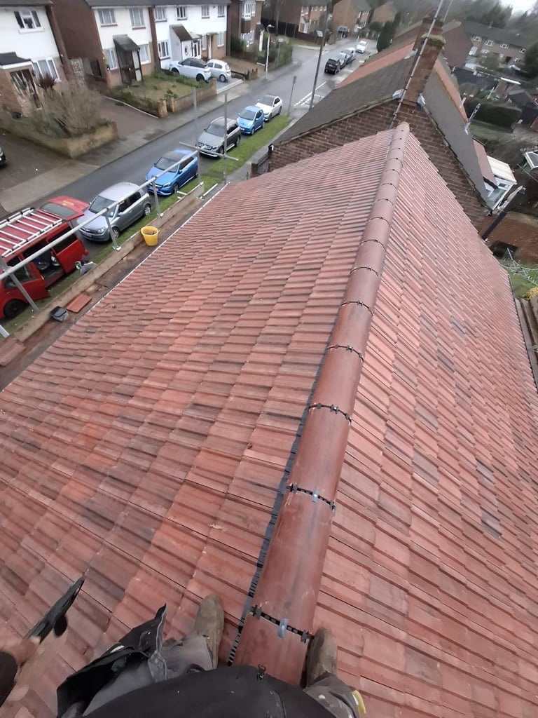 Aerial view of red clay tile roof with central chimney pipe, overlooking residential street with parked cars and houses