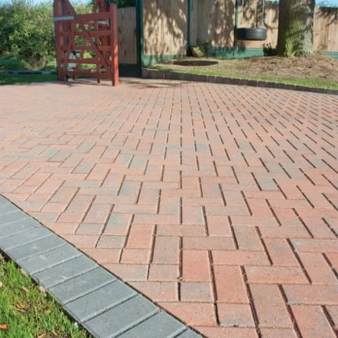 Herringbone pattern brick patio with red and gray pavers, red metal gate, and landscaped yard in background