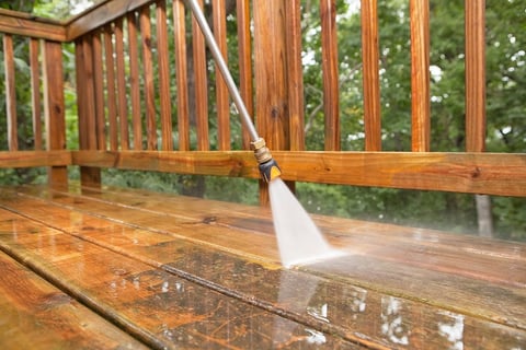 Person pressure washing a wooden deck
