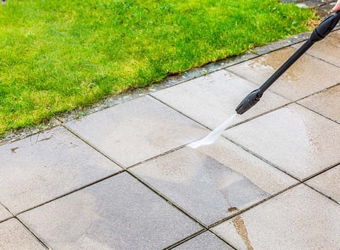 Person power washing a stone patio with green grass visible along the edge