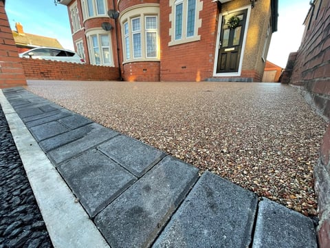 Modern driveway with dark paving stones and gravel surface leading to brick Victorian home