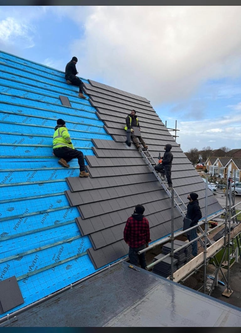 Construction workers installing roof tiles on a new residential building with blue protective sheeting and metal scaffolding