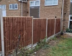 Brown corrugated metal fence installed along the side of a brick house with green lawn below